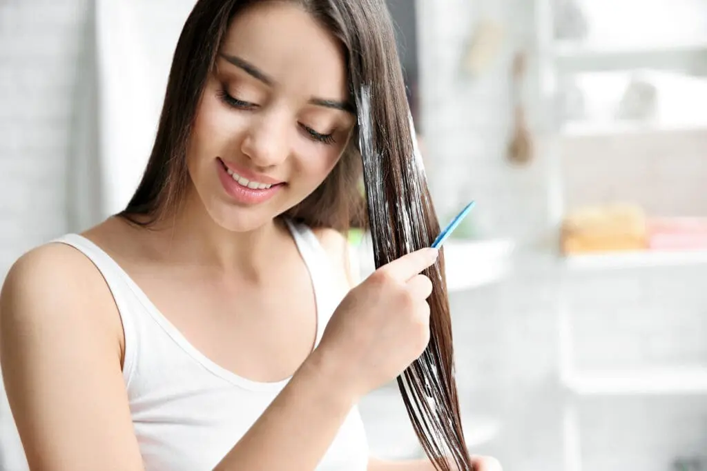Woman applies relaxer to her hair with a comb