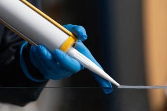 Clear sealant made with HSBC polymers for sealants is being applied to a reflective surface by a man wearing blue gloves.